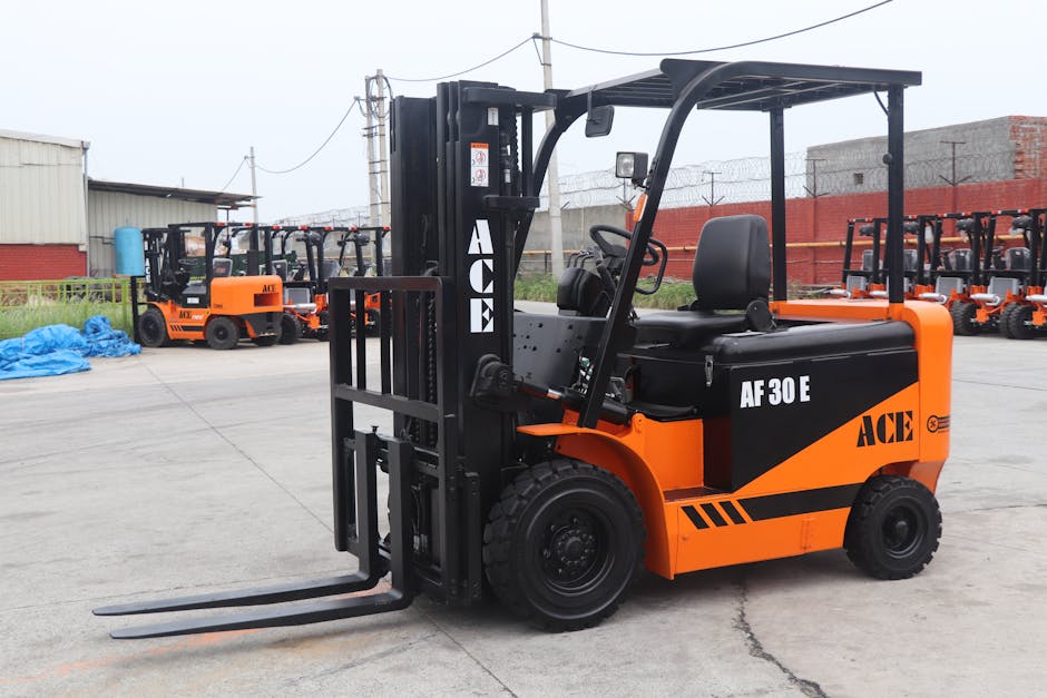 A close-up view of a small orange and black forklift with the label 'ACE AF30E,' positioned on a concrete surface at an industrial yard. In the background, multiple similar forklifts are lined up, wit